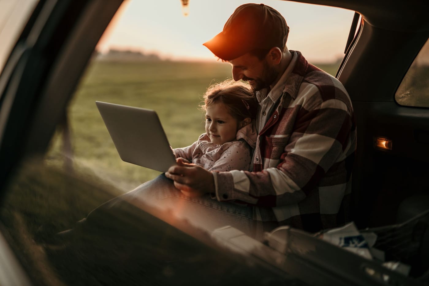 Bărbat cu un laptop în portbagajul deschis al unei mașini, la apus